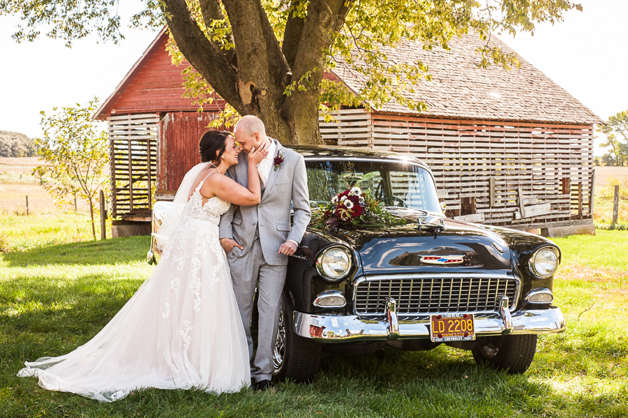 Barn in background with classic car and bride and groom